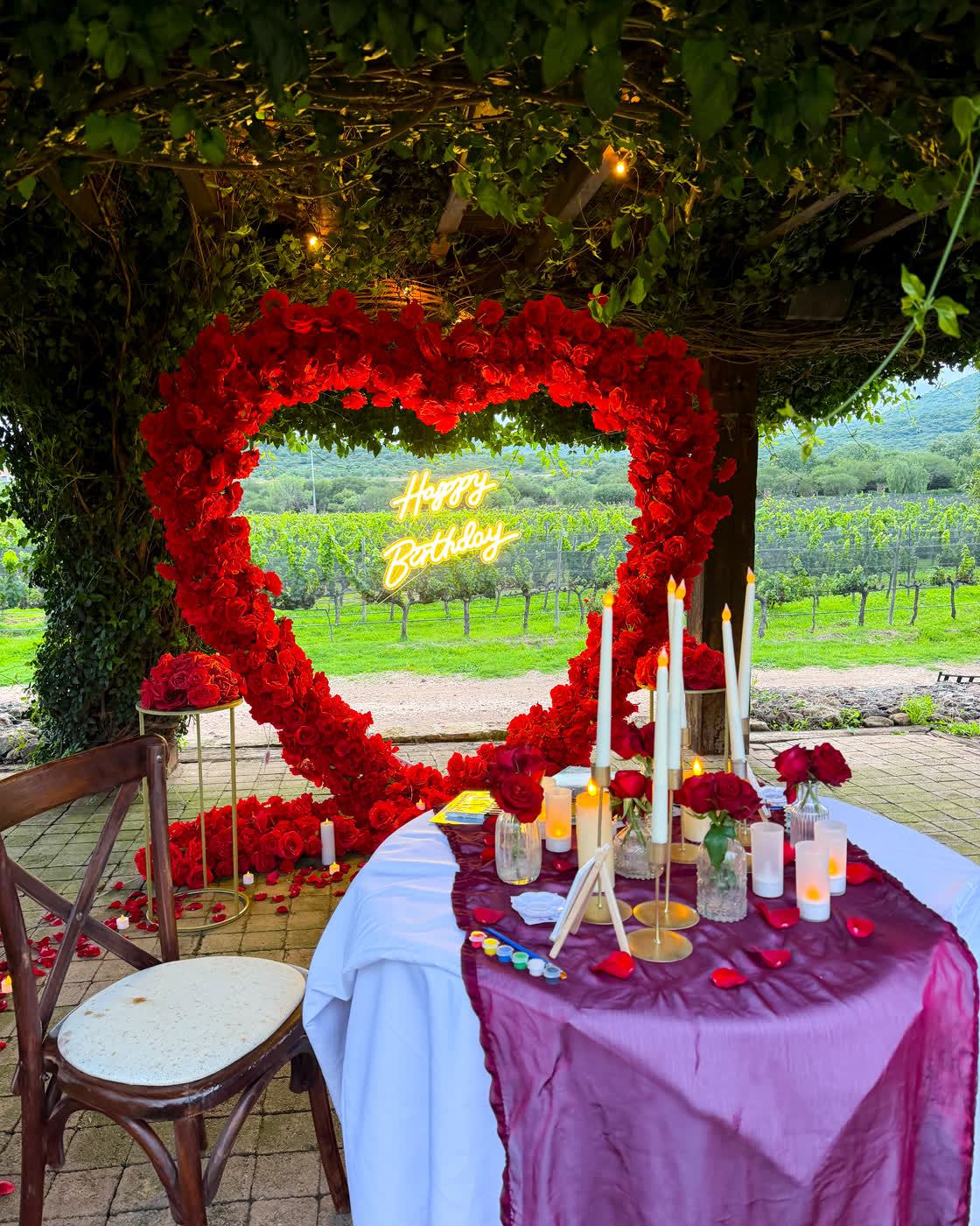 Corazón de rosas rojas con letrero Happy Birthday bajo enredadera en viñedo