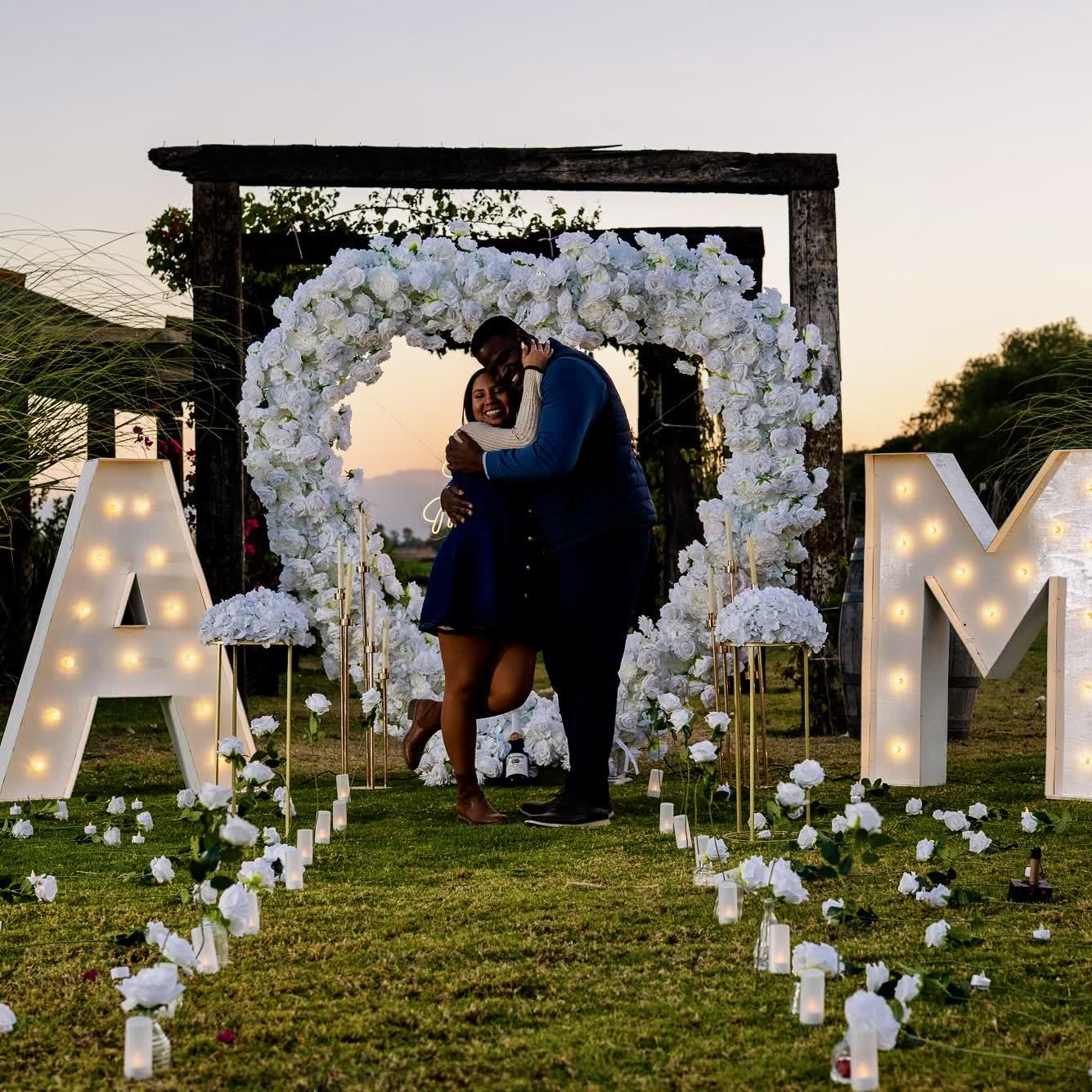 Corazón de rosas blancas con letras gigantes A y M al atardecer
