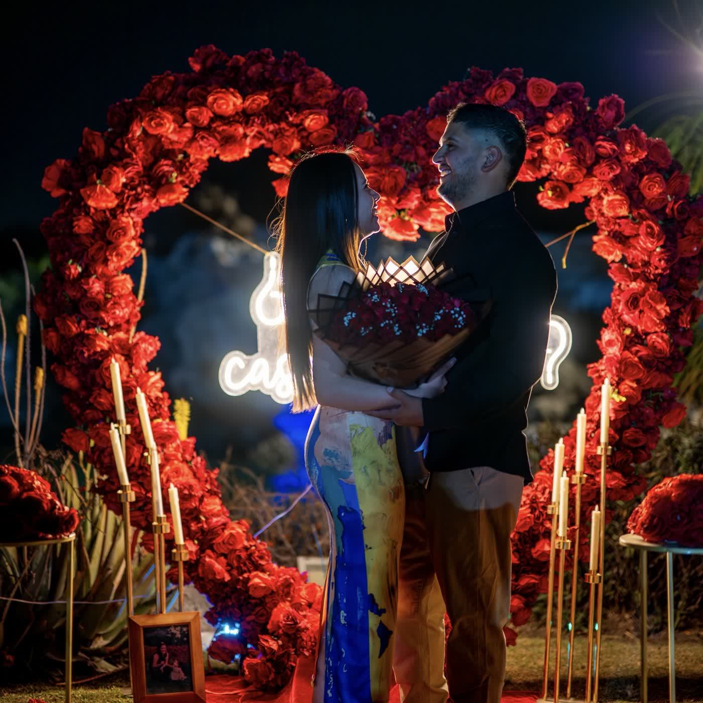 Corazón de rosas rojas con letrero neón de noche y pareja abrazada con ramo