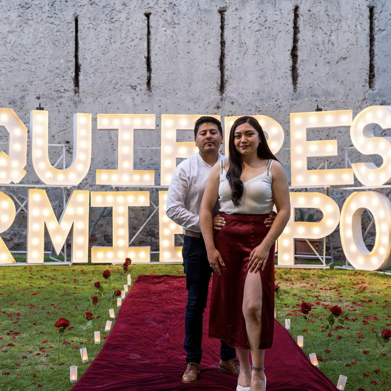 Letras gigantes iluminadas de propuesta de matrimonio con pareja abrazada