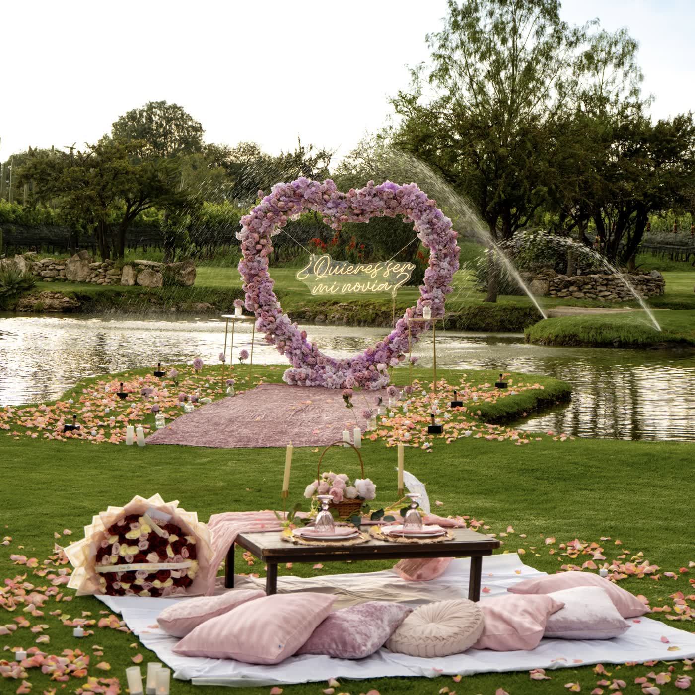 Corazón de rosas lila con picnic de cojines rosas junto al lago