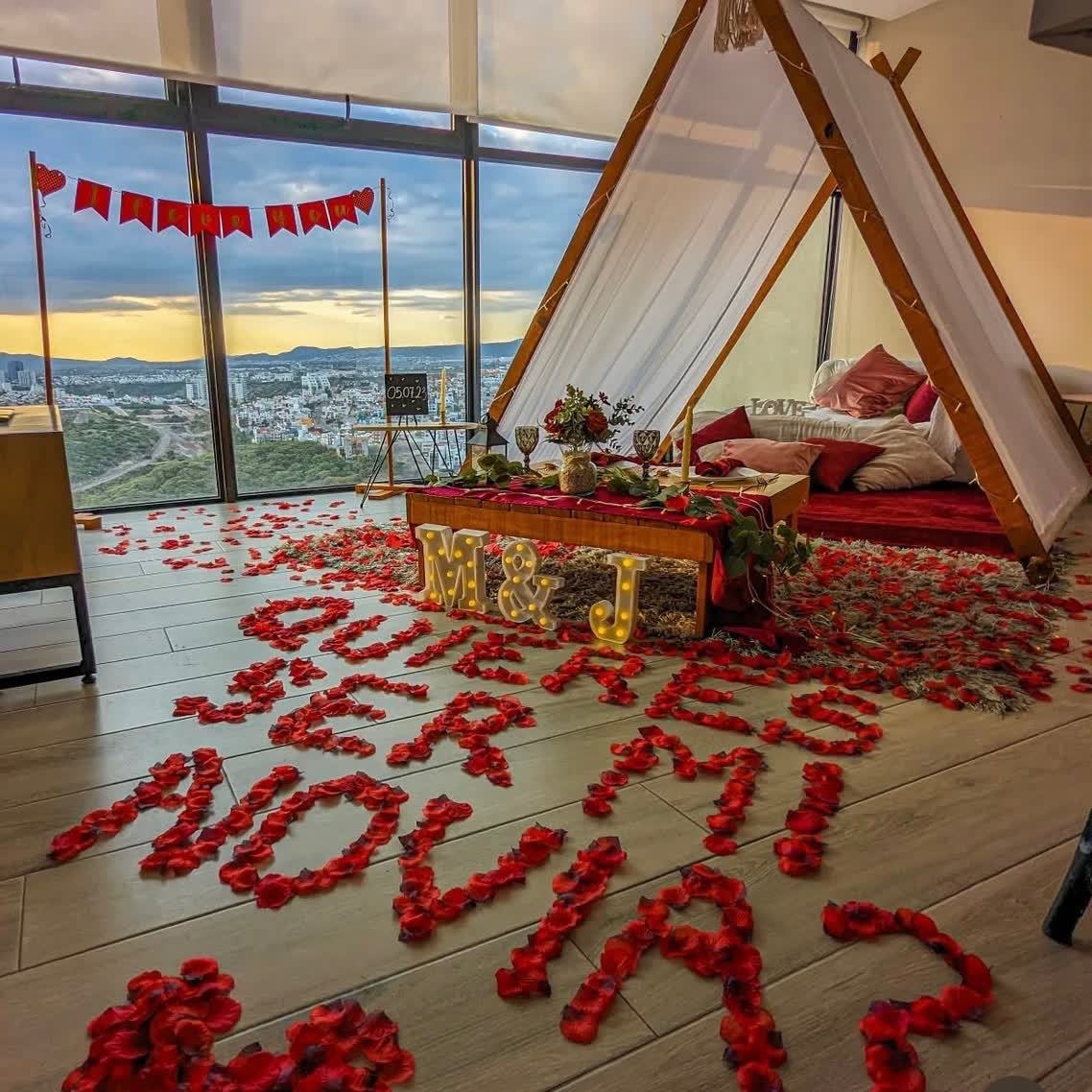 Pétalos de rosa formando QUIERES SER MI NOVIA en terraza con vista a la ciudad