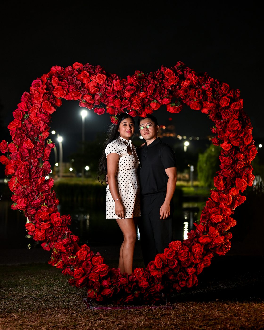 Kuma y Zoe abrazados dentro del corazón gigante de rosas rojas, de noche