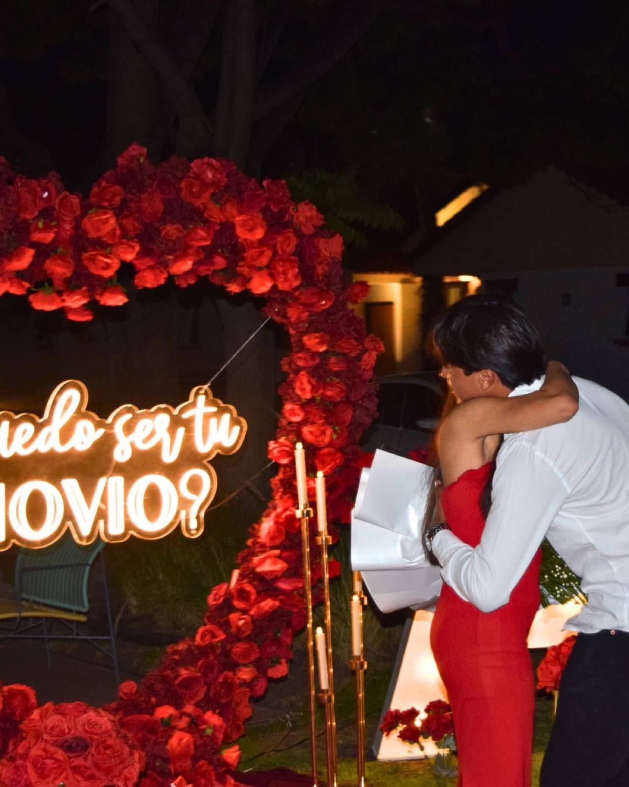 Pareja abrazada frente a corazón de rosas en pedida de noviazgo