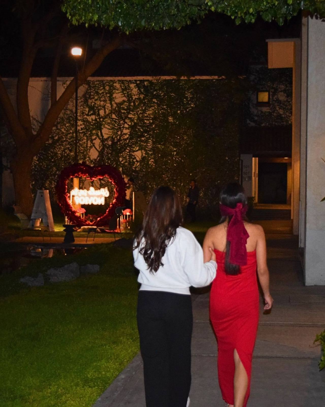 Pareja besándose con ramo de flores frente a corazón de rosas